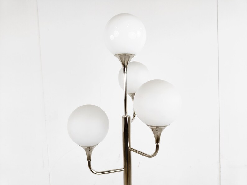 May include: A silver floor lamp with four white globe-shaped shades. The lamp has a modern design with a central pole and curved arms.