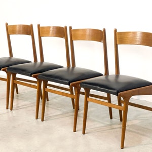 May include: Four mid-century modern dining chairs. The chairs have a light brown wooden frame with a curved backrest and black leather seats. The legs are tapered and angled, and the chairs are arranged in a row.