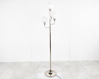 May include: A chrome floor lamp with five white globe-shaped shades. The lamp has a long, slender stem and a round base.