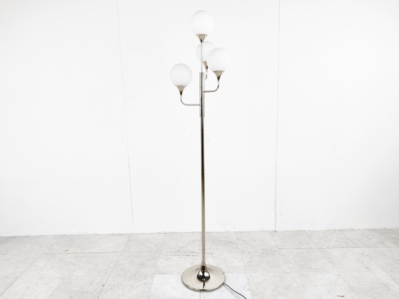 May include: A chrome floor lamp with five white globe-shaped shades. The lamp has a long, slender stem and a round base.