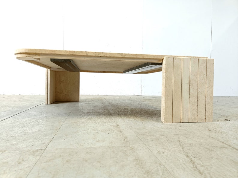 May include: A large, rectangular, travertine coffee table with a beveled edge and a slatted base. The table is made of natural stone and has a light beige color.