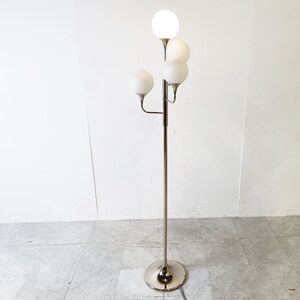 May include: A chrome floor lamp with five white globe-shaped shades. The lamp has a tall, slender base and a curved arm that extends to the side.