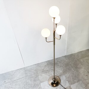 May include: A chrome floor lamp with five white globe-shaped shades. The lamp has a modern design with a central pole and branching arms.