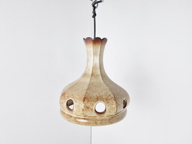 May include: A ceramic pendant light fixture with a brown and beige glaze. The light has a rounded, bulbous shape with a scalloped top and several circular cutouts.