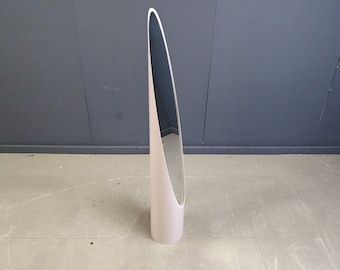 May include: A tall, modern floor mirror with a pale pink frame and a sleek, elongated oval shape. The mirror's reflective surface is visible within the frame, and it stands on a concrete floor against a dark gray wall. The mirror is approximately 60 inches tall.