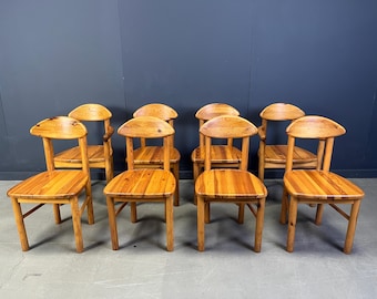 Puede incluir: Un conjunto de diez sillas de madera con acabado natural. Cada silla presenta un respaldo redondeado y un asiento cuadrado. Las sillas están dispuestas en grupo, mostrando su diseño sencillo pero robusto. La veta de la madera es visible.