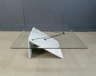 May include: A modern coffee table with a clear glass top and a white marble base. The base has a geometric design with angled supports. Black metal rods connect the base to the glass top. The table is approximately 48 inches long and 36 inches wide.
