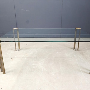 Puede incluir: Mesa de centro rectangular con tapa de cristal transparente y estructura metálica. Las patas son de color dorado claro y la mesa mide aproximadamente 122 cm de largo y 61 cm de ancho.