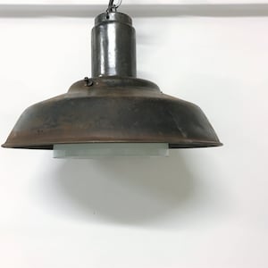 Pode incluir: Uma luminária pendente industrial de metal enferrujado com um difusor de vidro branco. A luz está pendurada em uma corrente.