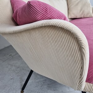 May include: A white and pink corduroy sofa with black legs. The sofa has a high back and a curved shape.