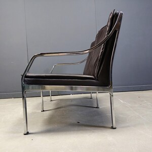 May include: A modern, two-seater sofa with a dark brown, leather-like seat and backrest. The frame is made of polished chrome, with armrests and four slender legs. The design is minimalist and sleek, suitable for a living room or office.