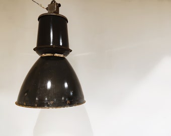 May include: A black industrial pendant light with a large, round shade and a smaller, cylindrical top. The light has a worn, vintage look.
