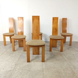 May include: Set of six wooden dining chairs with light brown upholstery. The chairs have a tall, slender back and a simple, modern design.