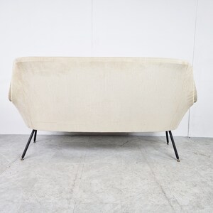 May include: A white, ribbed fabric sofa with black metal legs. The sofa has a curved back and a simple, modern design.