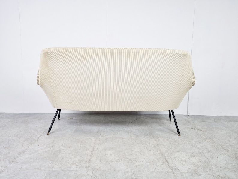 May include: A white, ribbed fabric sofa with black metal legs. The sofa has a curved back and a simple, modern design.