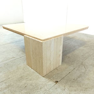 May include: A rectangular coffee table with a light beige travertine top and a base made of stacked travertine slabs. The table has a modern design and is perfect for a living room or den.