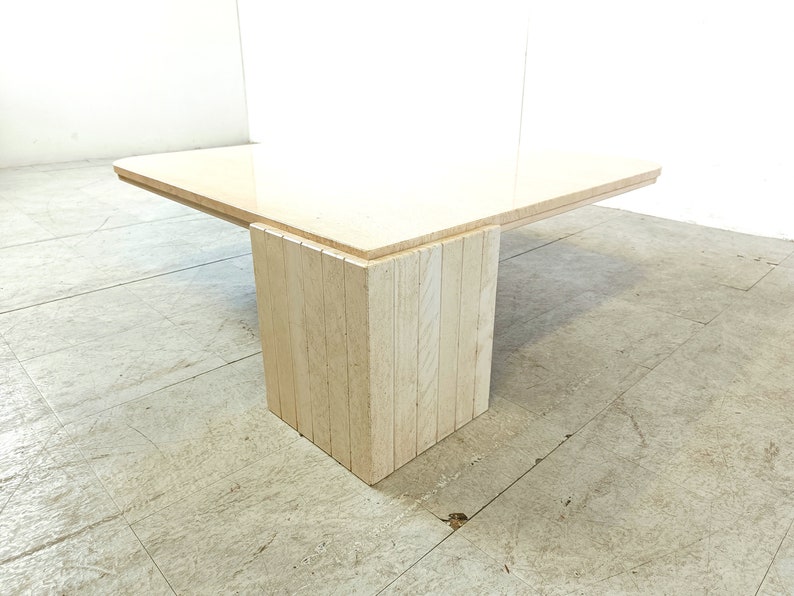 May include: A rectangular coffee table with a light beige travertine top and a base made of stacked travertine slabs. The table has a modern design and is perfect for a living room or den.