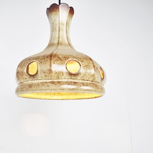 May include: A ceramic pendant light fixture with a brown and white glaze and round cutouts. The light is on and illuminating the room.