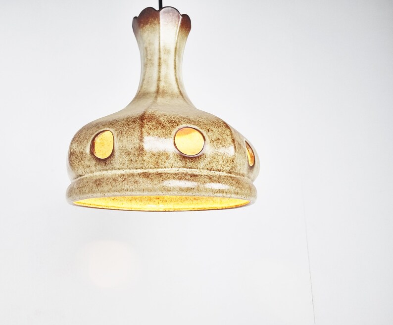 May include: A ceramic pendant light fixture with a brown and white glaze and round cutouts. The light is on and illuminating the room.