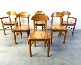 Puede incluir: Un conjunto de cinco sillas de madera con acabado marrón claro y veta visible. Las sillas presentan respaldos redondeados, asientos planos y cuatro patas. Dos de las sillas incluyen reposabrazos, mientras que tres no tienen.
