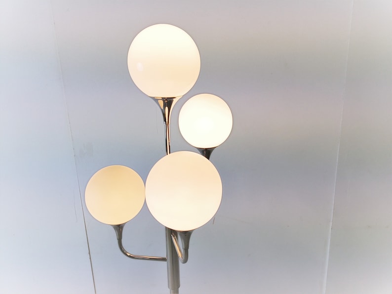 May include: A chrome floor lamp with four white globe-shaped light shades. The lamp has a modern design with a sleek, minimalist aesthetic.