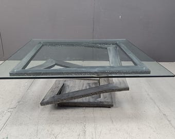 May include: A modern coffee table with a glass top and a geometric metal base. The base is made of several pieces of metal that are joined together in a unique way.