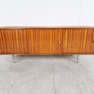 May include: A mid-century modern sideboard with four doors and metal legs. The cabinet is made of wood with a rich brown finish and has a horizontal grain pattern.