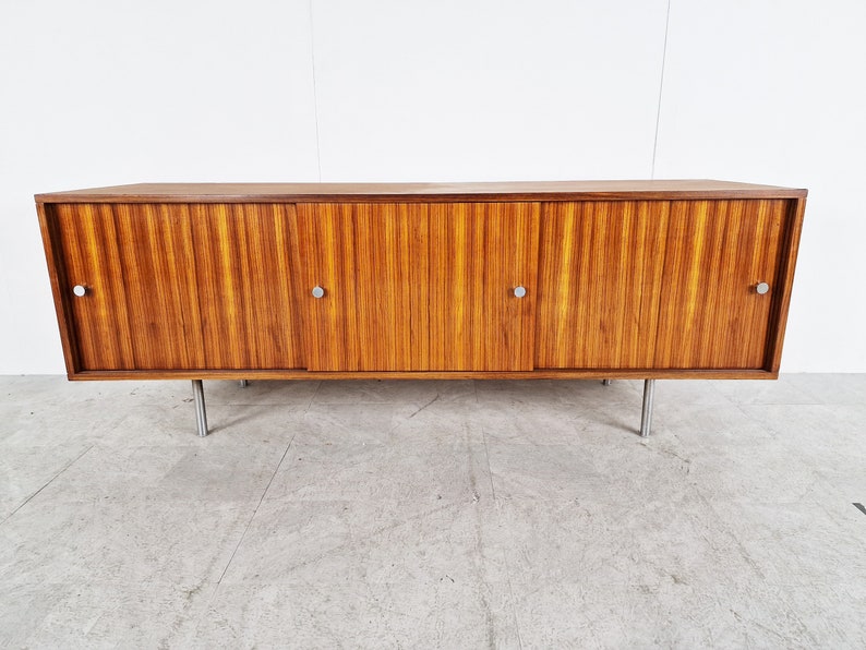 May include: A mid-century modern sideboard with four doors and metal legs. The cabinet is made of wood with a rich brown finish and has a horizontal grain pattern.