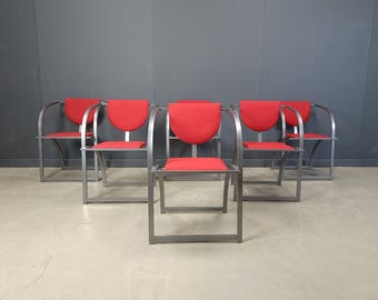 May include: Six modern chairs with a red seat and backrest. The chairs have a silver metal frame with curved armrests. The chairs are arranged in a row, with the backs of the chairs facing the viewer.