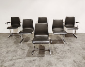 May include: Six black leather chairs with chrome legs and arms. The chairs are arranged in a row on a grey tiled floor.