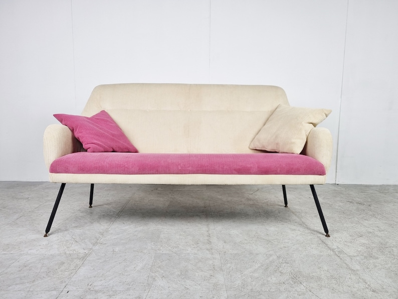 May include: A white and pink two-seater sofa with black legs. The sofa has two pillows, one pink and one white.