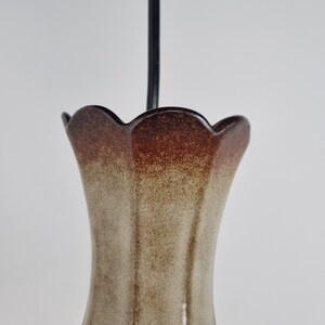 May include: A brown and beige ceramic vase with a scalloped rim. The vase has a speckled glaze and a gradient of color from brown to beige.