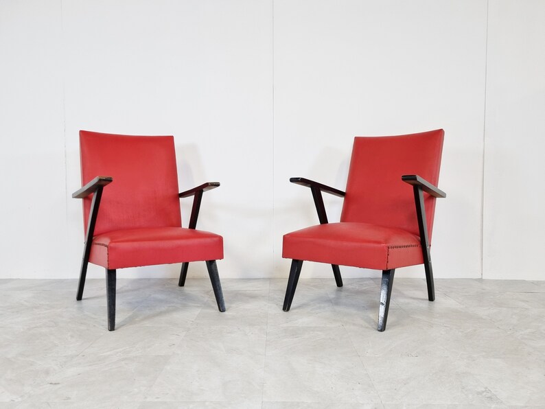 May include: Two red armchairs with black wooden frames. The chairs have a simple, mid-century modern design.