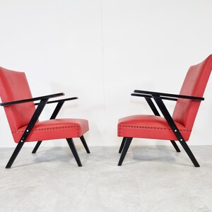 May include: Two red chairs with black wooden frames. The chairs have a simple design with angled legs and arms.