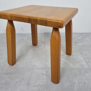 Puede incluir: Una peque&ntilde;a mesa auxiliar cuadrada de madera con cuatro patas torneadas. La mesa est&aacute; hecha de madera marr&oacute;n claro y tiene un dise&ntilde;o simple y r&uacute;stico.