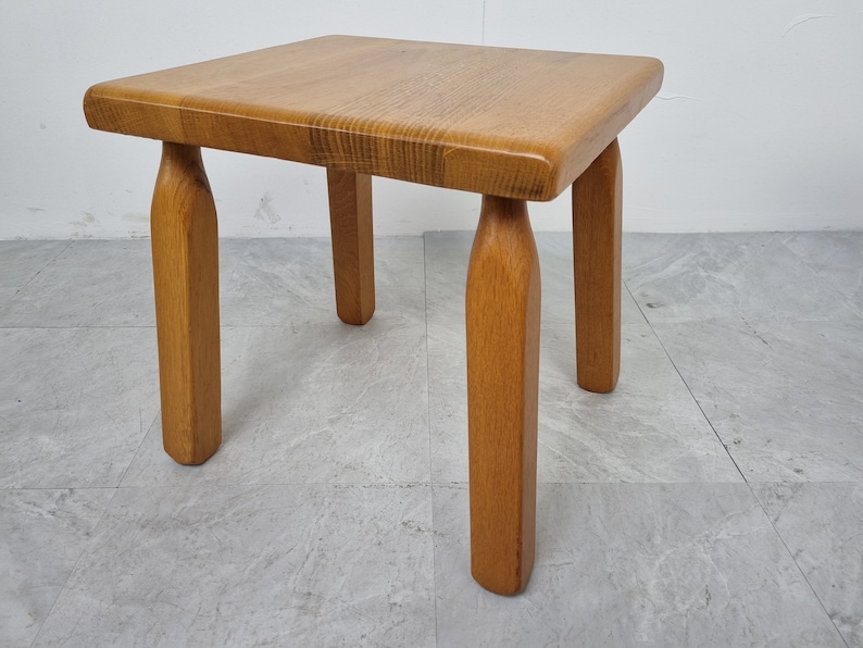 Puede incluir: Una peque&ntilde;a mesa auxiliar cuadrada de madera con cuatro patas torneadas. La mesa est&aacute; hecha de madera marr&oacute;n claro y tiene un dise&ntilde;o simple y r&uacute;stico.