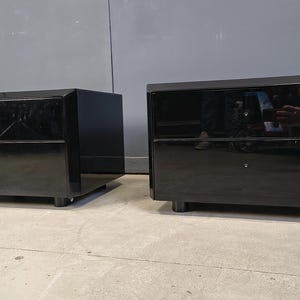 May include: Two matching black nightstands with a glossy finish. Each nightstand has two drawers and sits on short, rounded legs. The design is modern and sleek, suitable for a bedroom setting.