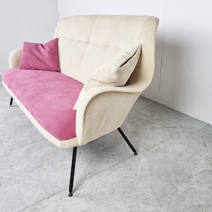 May include: A white and pink corduroy sofa with black metal legs. The sofa has two pillows, one pink and one white.