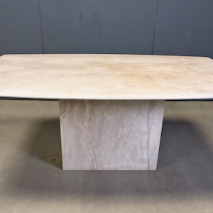 Op de afbeelding: Een rechthoekige stenen tafel met een lichtbeige blad en een massieve, getextureerde basis. De tafel heeft een modern design en is geschikt voor diverse interieurs. De afmetingen van de tafel zijn ongeveer 183 cm lang, 91 cm breed en 76 cm hoog.
