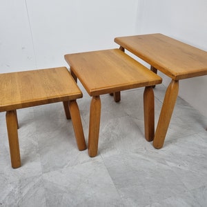 Puede incluir: Conjunto de tres mesas nido de madera con acabado natural. Las mesas son cuadradas y tienen cuatro patas cada una. La mesa m&aacute;s grande est&aacute; en el fondo, y la mesa m&aacute;s peque&ntilde;a est&aacute; en primer plano.