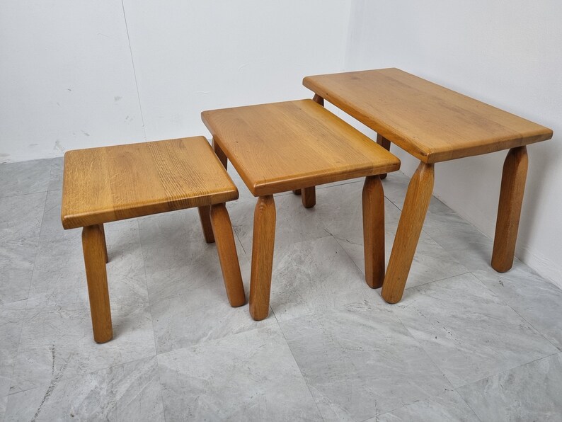 Puede incluir: Conjunto de tres mesas nido de madera con acabado natural. Las mesas son cuadradas y tienen cuatro patas cada una. La mesa m&aacute;s grande est&aacute; en el fondo, y la mesa m&aacute;s peque&ntilde;a est&aacute; en primer plano.