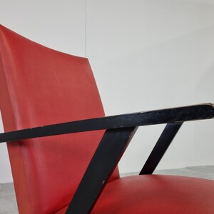 May include: A red upholstered armchair with black wooden arms and a geometric design. The chair has a curved back and a wide seat.