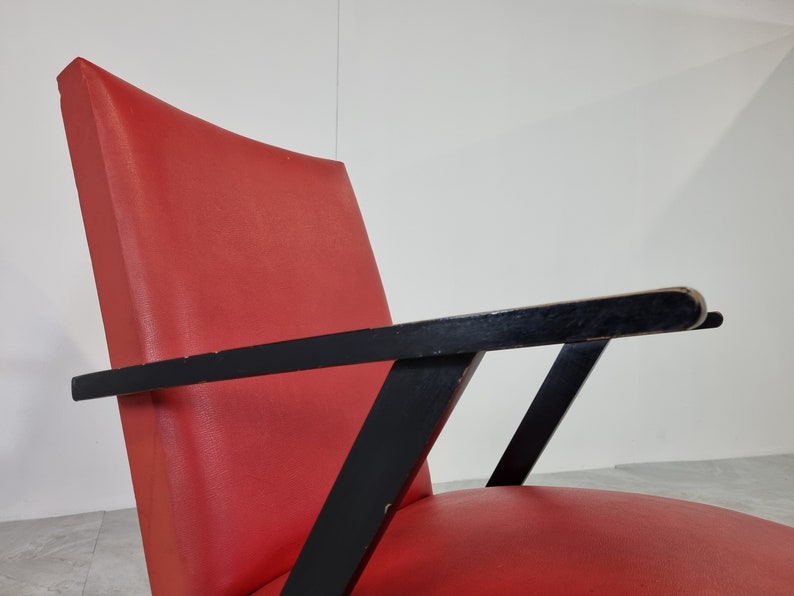 May include: A red upholstered armchair with black wooden arms and a geometric design. The chair has a curved back and a wide seat.