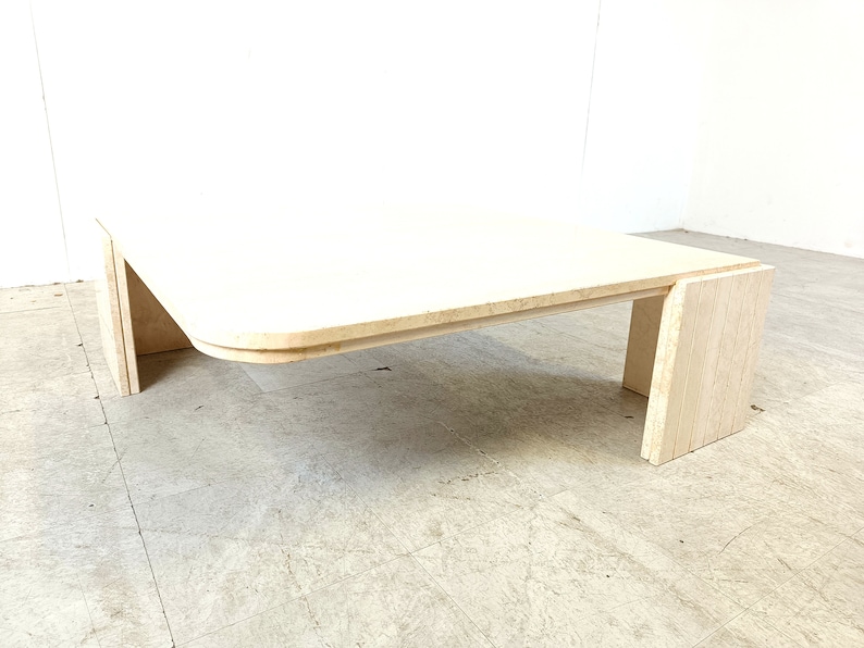 May include: A white travertine coffee table with a curved top and a rectangular base. The table is made of natural stone and has a unique, organic look.
