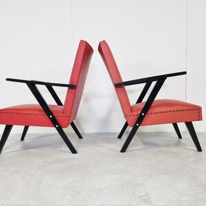 May include: Two red armchairs with black wooden frames. The chairs have a simple, mid-century modern design.