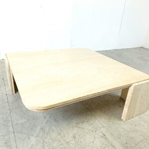 May include: A square, light-colored wood coffee table with rounded edges and a unique, layered base.