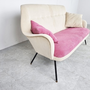 May include: A white and pink fabric sofa with black metal legs. The sofa has a tufted back and a pink cushion.