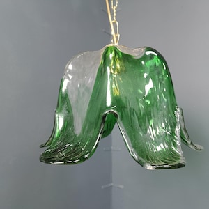 Pode incluir: Um pendente de luz de vidro verde em forma de flor com um centro de vidro transparente.