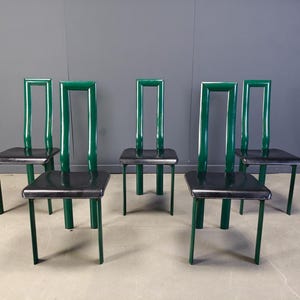 May include: Six green chairs with black square seats. The chairs have a distinctive design with a rectangular back and thin legs. The chairs are arranged in a row, showcasing their modern aesthetic.