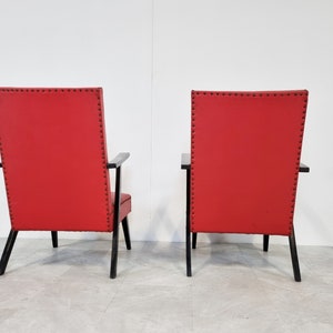 May include: Two red chairs with black wooden frames and black upholstery tacks. The chairs are facing away from the camera.